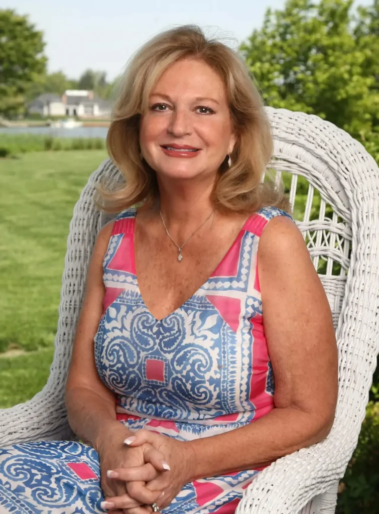 Elegant woman in a patterned dress sits in a white wicker chair outdoors.