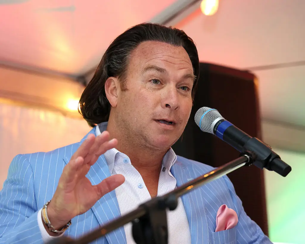 Man in blue suit speaking into microphone, gesturing with hand.