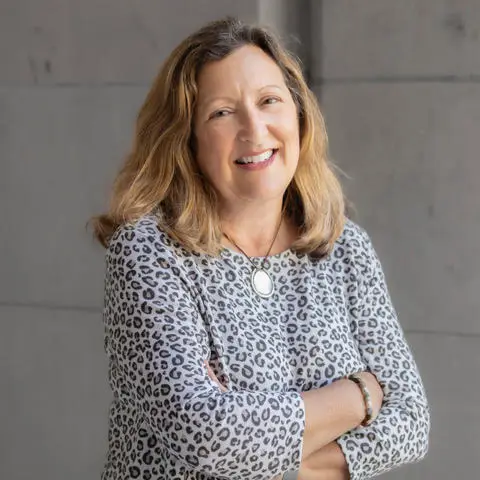 Portrait of a smiling woman with arms crossed wearing a leopard print top.