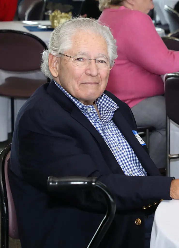 Older gentleman in a blue blazer and checkered shirt smiling at an event.