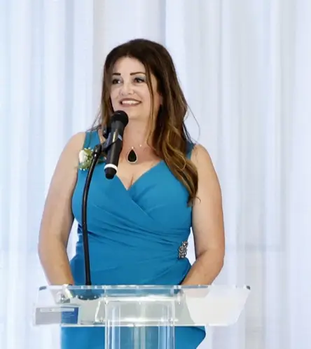Woman in teal dress giving a speech at a podium.