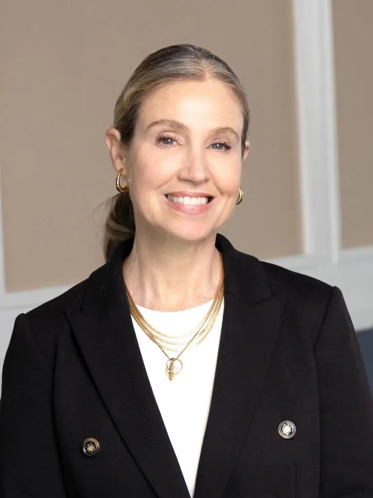 Woman smiling in a black blazer and gold jewelry.