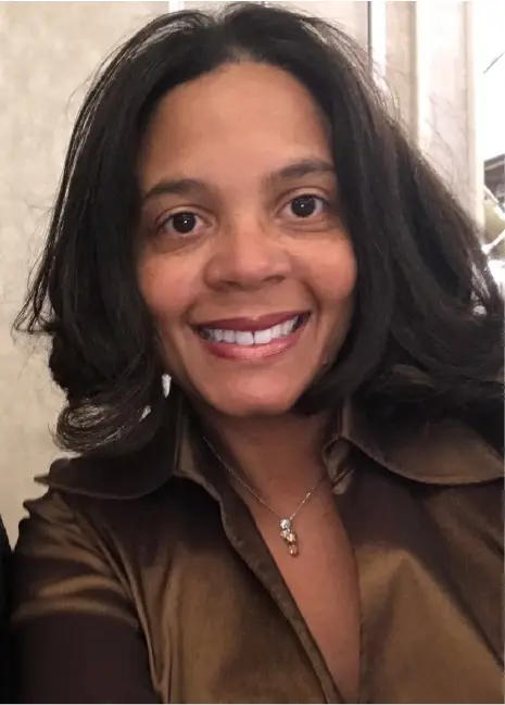 Smiling woman with dark hair wearing a brown satin shirt and a necklace.