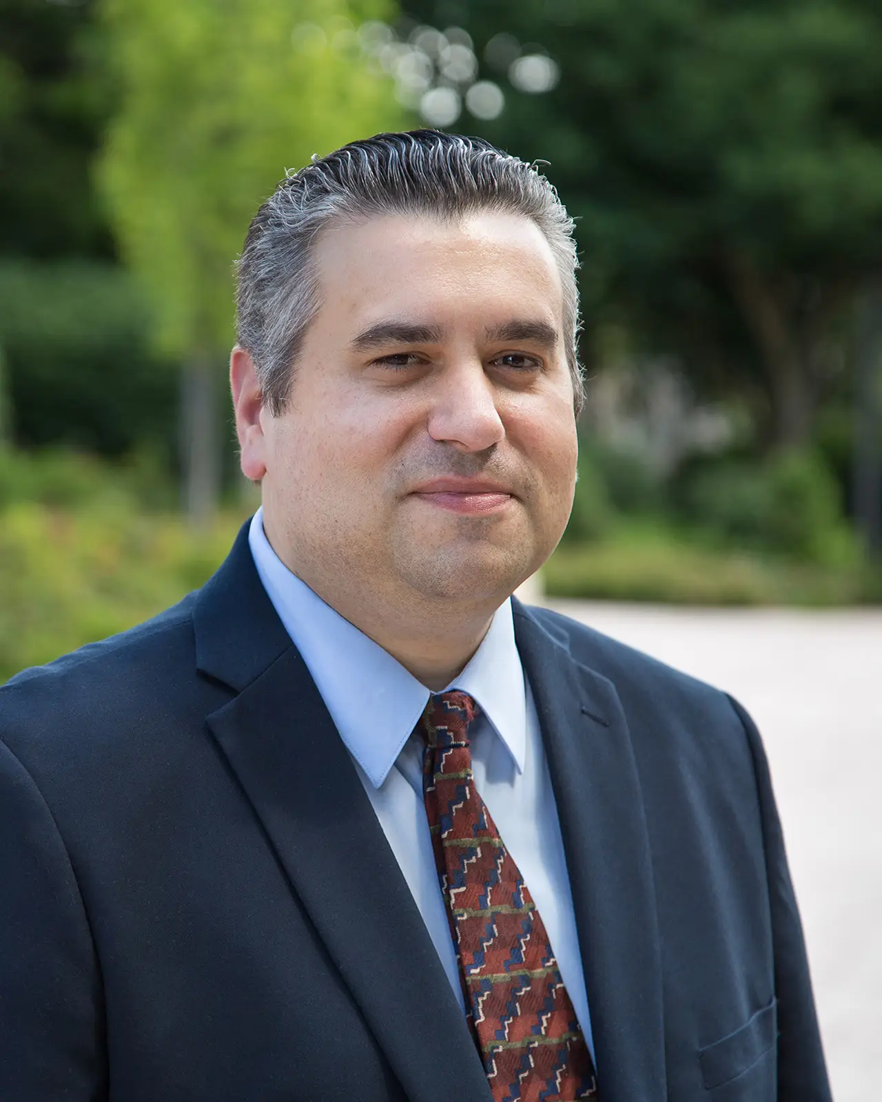 Man in a dark suit, light blue shirt, and patterned tie.