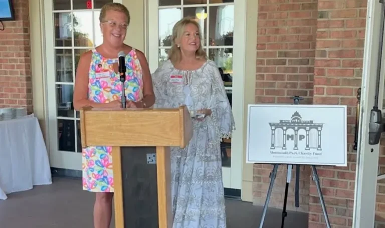Two women stand near a podium with a Monmouth Park Charity Fund sign.