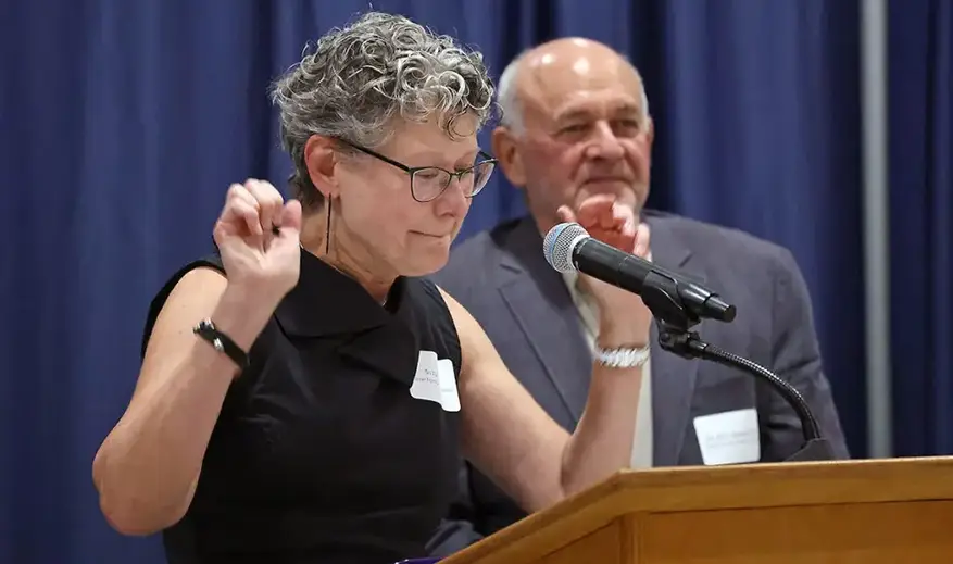 Woman speaks at podium with man behind her
