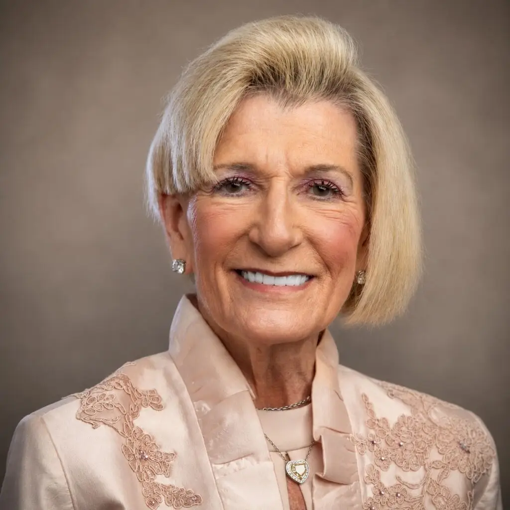 Elderly woman with blonde hair and a pink jacket smiles warmly